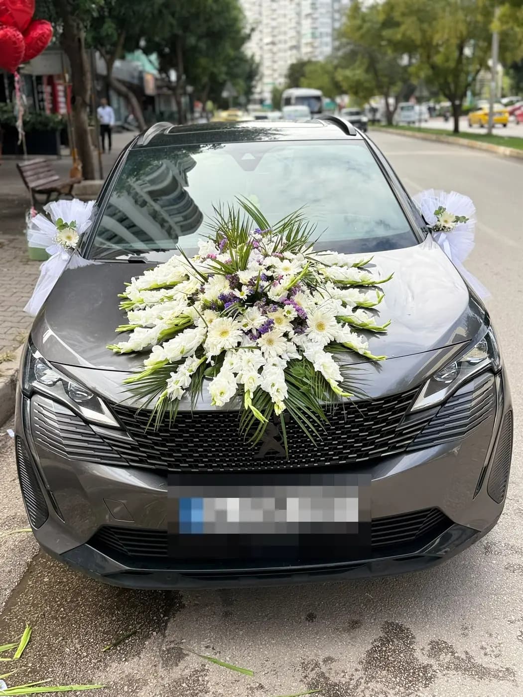Gri Peugeot aracın kaputunda beyaz krizantemlerle yapılmış gelin arabası süslemesi