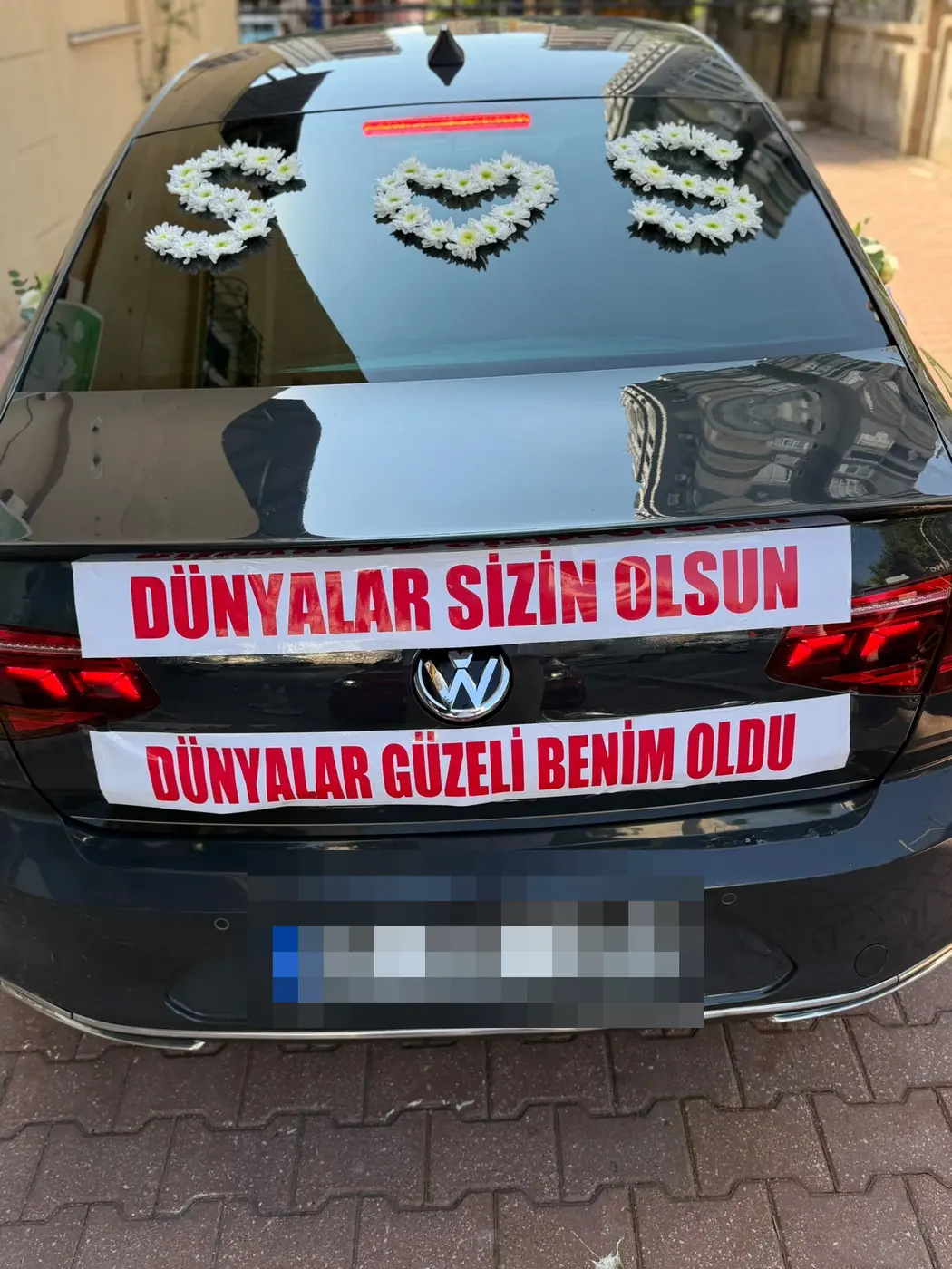 Siyah VW aracın arka camında beyaz çiçek süslemeleri ve yazılı pankartlar
