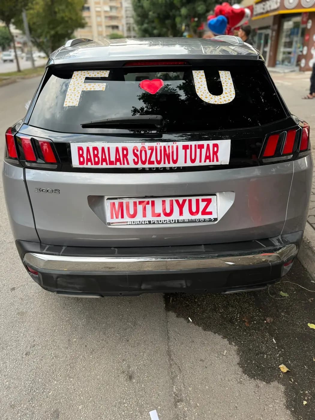 Gümüş Peugeot aracın arka camında çiçek harfleri ve 'Babalar sözünü tutar' yazılı pankart