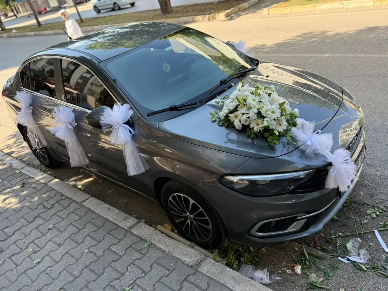 Gri sedan aracın kapılarında tül fiyonklar ve kaputta beyaz çiçek buketi