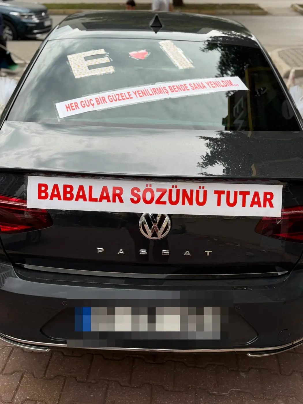 Siyah VW aracın arka camında çiçek harfleri ve 'Babalar sözünü tutar' pankartı